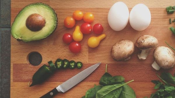 Avocado, tomatoes, eggs, mushrooms, and spinach on a cutting board