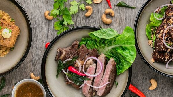 Plates of sliced steak with greens and side dishes on a wooden table
