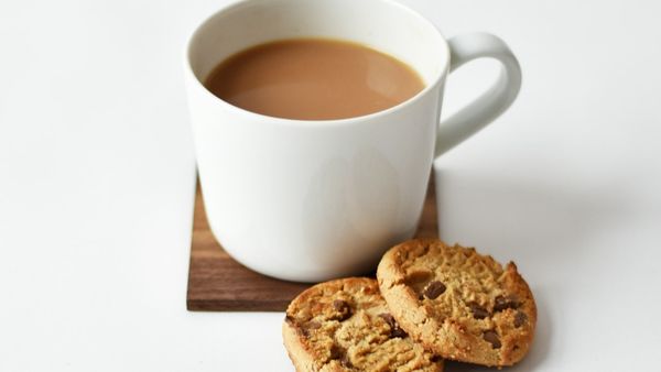 A mug of milky tea with two cookies on a wooden coaster