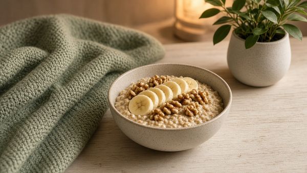 Bowl of oatmeal with banana and walnuts beside a soft sage blanket