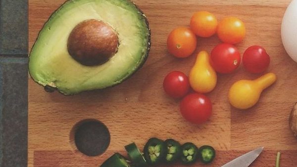 Halved avocado with cherry tomatoes and sliced jalapeño on a wooden board