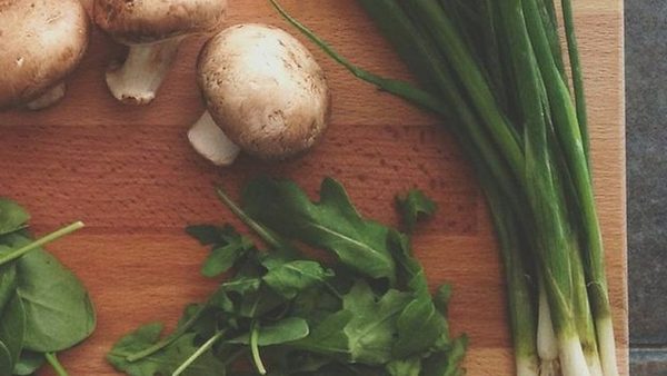 Leafy greens, scallions, and mushrooms on a wooden board