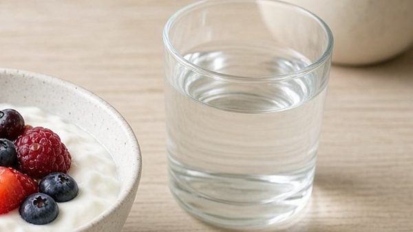 A glass of water beside a bowl of yogurt topped with berries