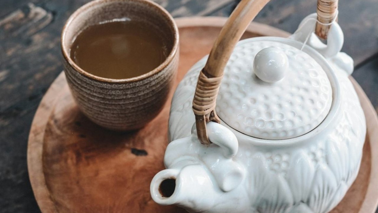 A cup of tea on a wooden tray beside a white teapot