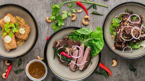 Shared plates of sliced steak, greens, and a sauced side on a wooden table
